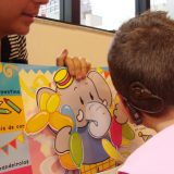 Imagem da fono Lilian mostrando o livro infantil, com um desenho de elefante em dobradura para o pequeno usuário do implante coclear, que aparece preso à cabeça dele.
