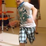 Um menino de cerca de 7 anos aparece correndo e sorrindo. A foto está meio borrada, pelo movimento de corrida dele.