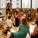 Imagem do pessoal: crianças, mães e equipe, sentados no chão, debatendo sobre o último dia do semestre.
