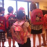 Imagem das crianças, de costas, mostrando as respectivas mochilas que ganharam de presente na festa de natal