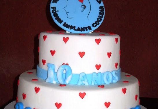 Imagem de bolo de dois andares, com o logo do FIC (um perfil de rosto com um aparelho em forma de coração no lugar da parte externa do implante). O bolo está decorado com corações e a frase 10 anos - 2001 - 2011