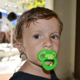 Usuario do Implante Coclear, de 2 anos, posa para a foto com o IC aparecendo numa das orelhas. Ele está serio e chupa chupeta verde.