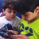Miguel e Guilherme, ambos irmãos de crianças implantadas, brincam com um gameboy durante o evento.