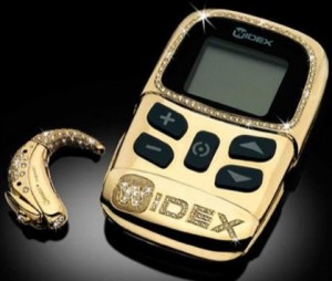 Imagem de um aparelho auditivo extraauricular feito em ouro e diamantes, acompanhado com aparelho de regulagem, também feito com o mesmo material.
